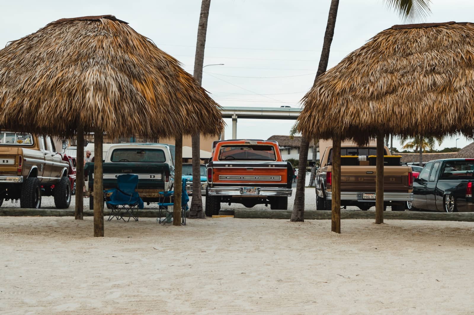 Trucks parked in the shade of thatched tiki huts on the sand